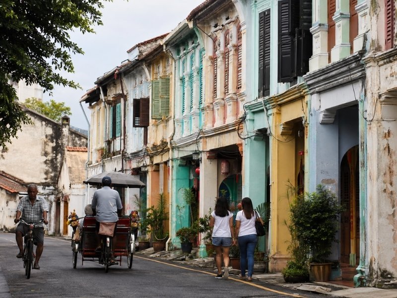 Colourful heritage shophouses, pedestrians and a trishaw in George Town, Penang