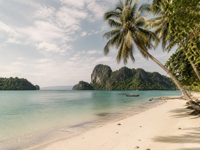 Perhentian Islands beach with turquoise water, forested hills, granite rocks and a traditional boat