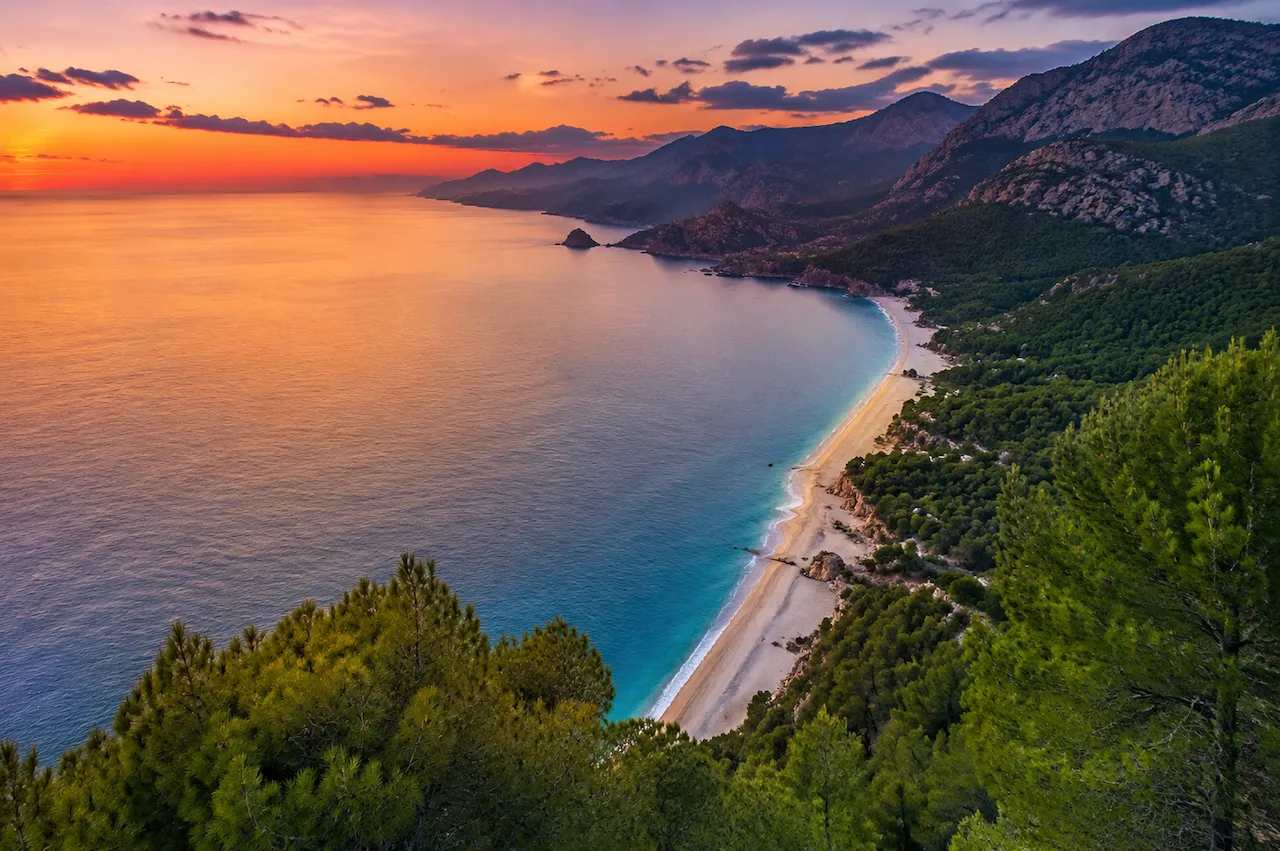 Sunset over a long beach bordered by pine-covered mountains on the Antalya coast.