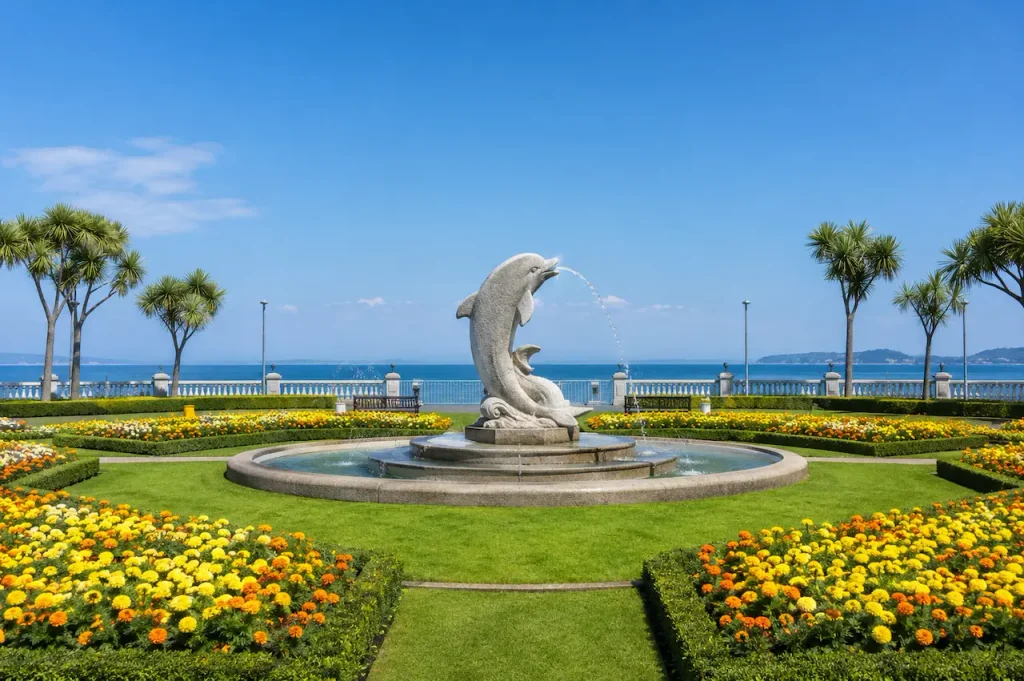 Dolphin fountain surrounded by colourful flower beds in a seaside garden in Antalya.
