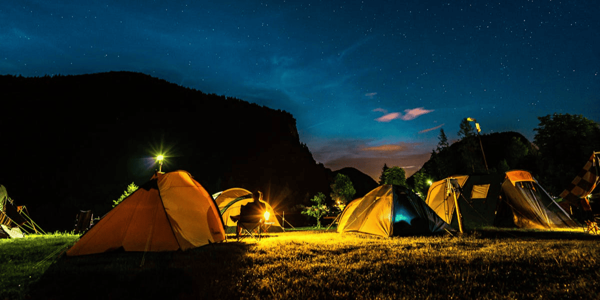 Scenic nighttime campsite with tents and lanterns under a bright starry sky