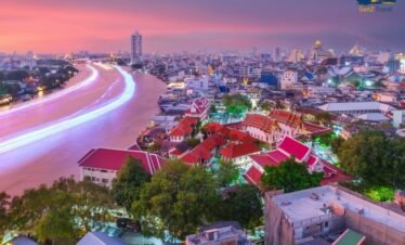 Modern luxury hotel suite overlooking Bangkok skyline at night with glowing city lights and river view
