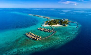 Aerial view of Centara Ras Fushi Resort Maldives with turquoise lagoon, overwater villas, and tropical island scenery.