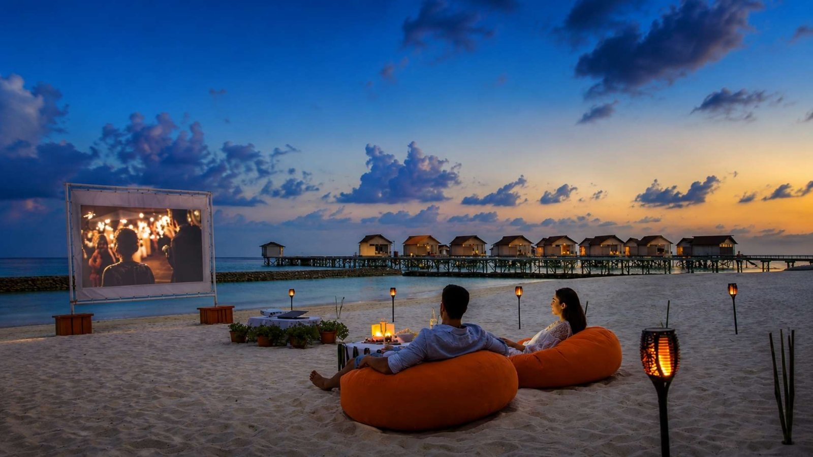 Couples relaxing on bean bags during a romantic beach movie night at a Maldives adults-only resort.