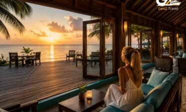 UK female traveller sitting on a teal-cushioned sofa in an open-air lounge at Canareef Resort Maldives, enjoying the ocean sunset view.