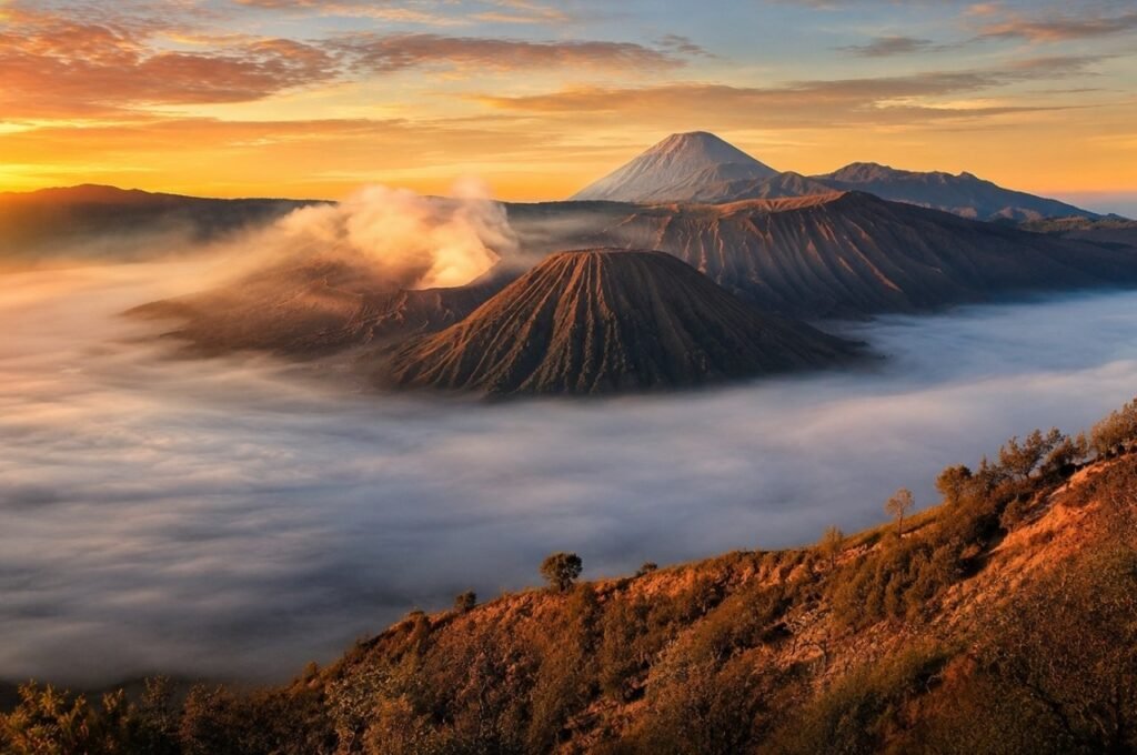 Mount Bromo volcanic landscape rising above clouds and mist during a golden sunrise in Indonesia.