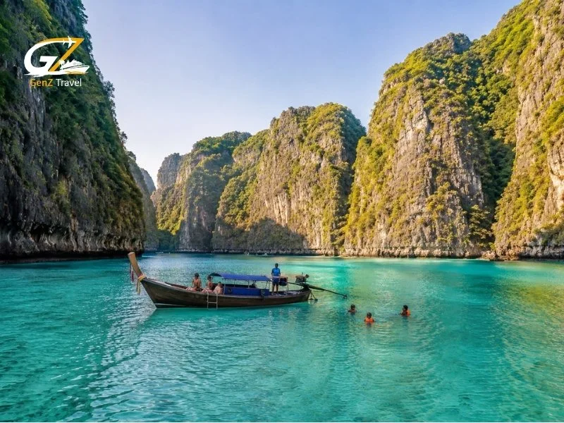 Things to do in Phi Phi, with travellers swimming beside a traditional long-tail boat in a turquoise lagoon surrounded by limestone cliffs.