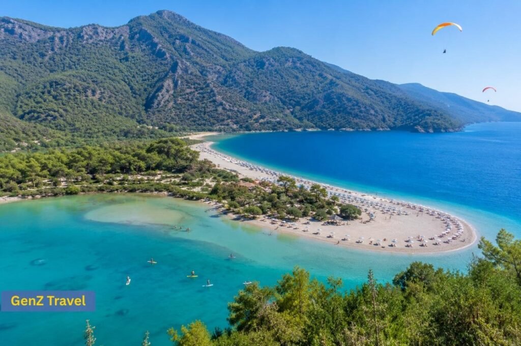 Aerial view of Ölüdeniz Blue Lagoon with turquoise water, curved beach, forested mountains and paragliders