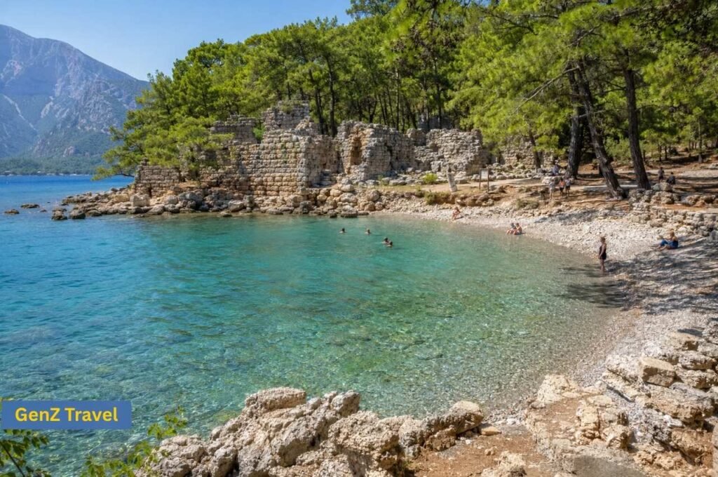 Clear turquoise bay at Phaselis Beach with ancient stone ruins, pine trees and a pebbled shoreline