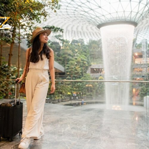 Female traveller with suitcase inside Jewel Changi Airport Singapore beside the indoor Rain Vortex waterfall