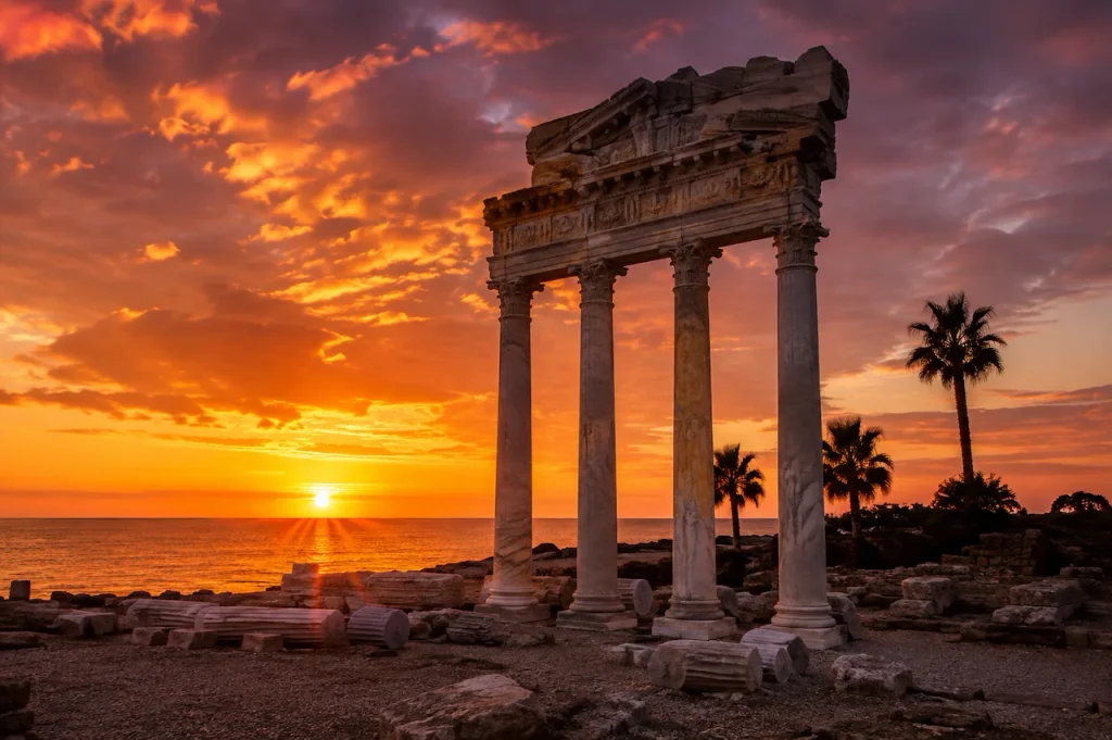 Ancient columns of the Temple of Apollo in Side silhouetted against a Mediterranean sunset.