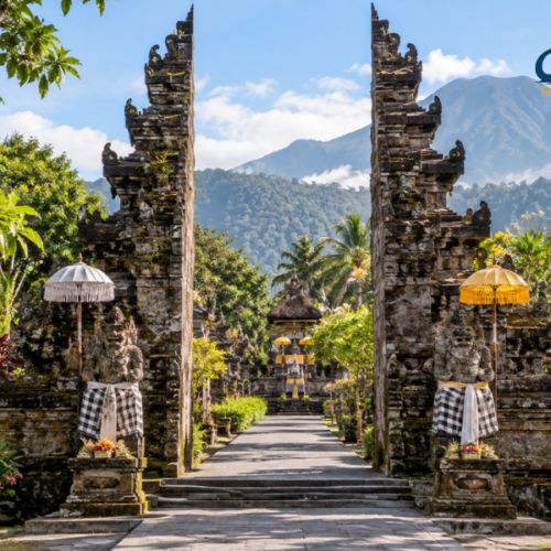 Traditional Balinese temple entrance with carved stone gates, guardian statues, tropical gardens and mountains in the background.