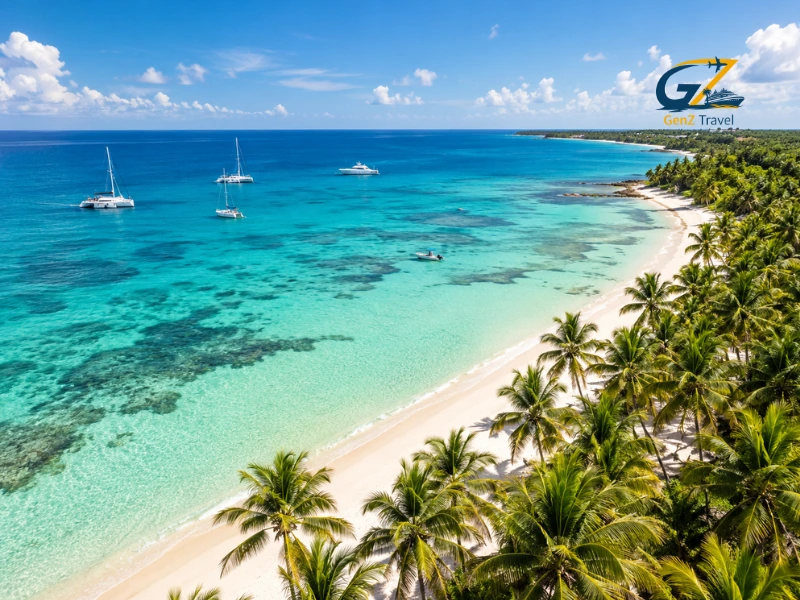 Aerial view of a Caribbean tropical coastline with turquoise waters, white-sand beaches, palm trees and luxury yachts.