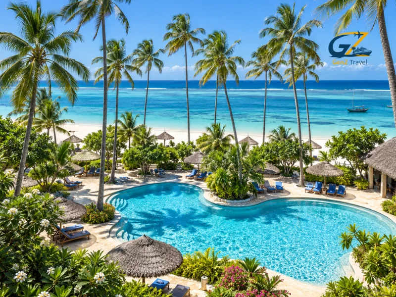 Zanzibar all-inclusive holiday resort featuring a tropical swimming pool, tall palm trees, sun loungers and turquoise Indian Ocean views.