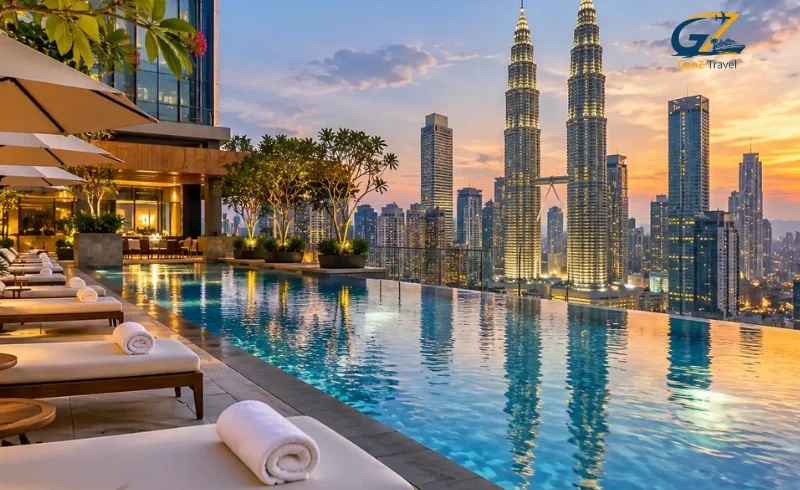 Luxury hotel rooftop infinity pool in Kuala Lumpur with sun loungers and stunning views of the illuminated Petronas Twin Towers at sunset.