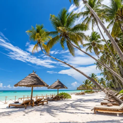 Beautiful Zanzibar beach with white sand, turquoise Indian Ocean water, palm trees and traditional thatched beach umbrellas.